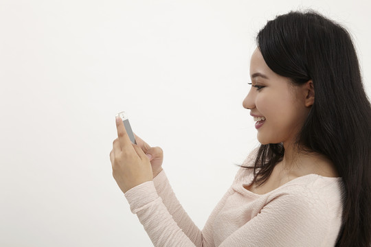 快乐美丽的年轻女子短信和上网与她的智能手机隔离在白色背景