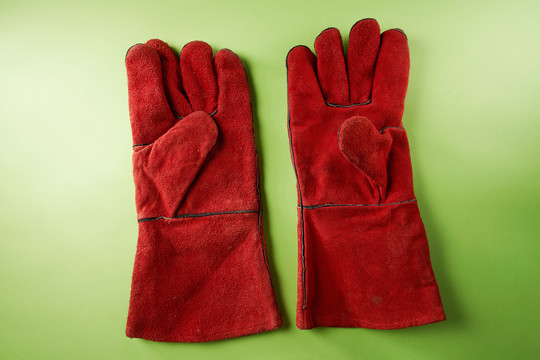 一双红色的皮革工作手套，隔离在绿色背景上。