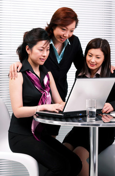 三个穿着西装的女人共用一台笔记本电脑