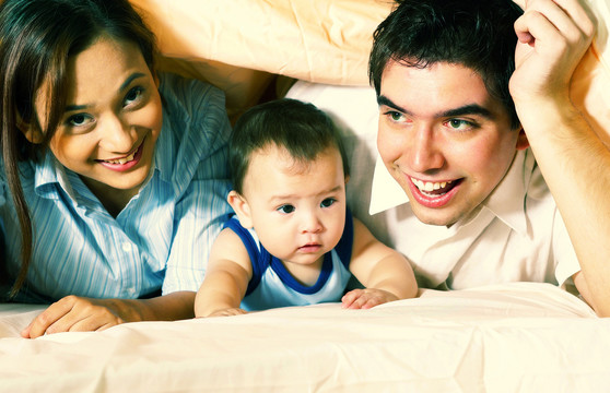 一对夫妇和他们的小儿子躲在毯子下面