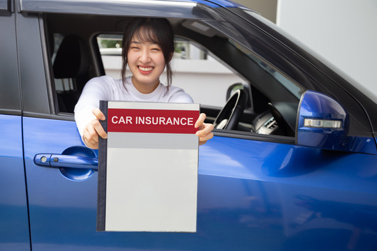 快乐亚洲女性持有汽车保险文件簿，坐在车内，安全车和保护客户人的理念
