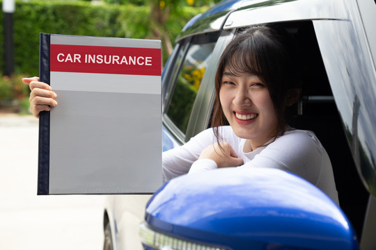快乐亚洲女性持有汽车保险文件簿，坐在车内，安全车和保护客户人的理念