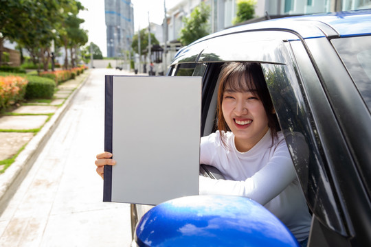年轻的亚洲女性持有保单汽车簿，坐在车内，个人意外保险理念