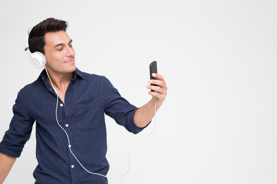 英俊的白人年轻男子戴着耳机在智能手机上听音乐，青少年在手机上播放音乐列表，在网站上享受顶级音乐流媒体
