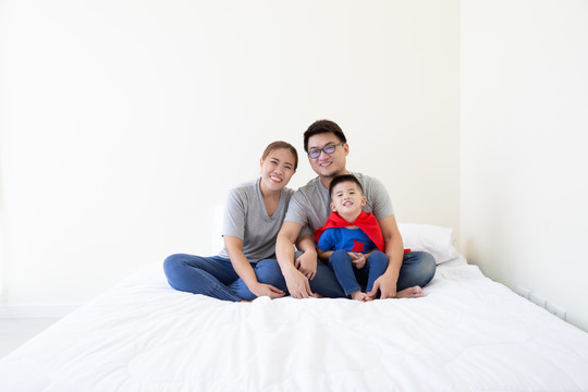 亚裔父亲、母亲和儿子在卧室的床上扮演超级英雄。友好的家庭玩得开心