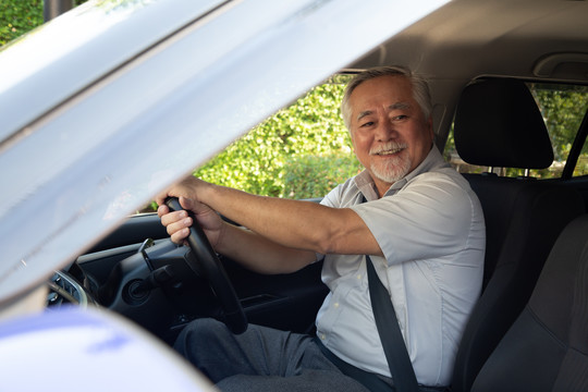 亚洲资深男士在开车旅行的过程中，开心地微笑着，带着快乐的积极表情，人们享受着欢笑的交通和轻松快乐的成