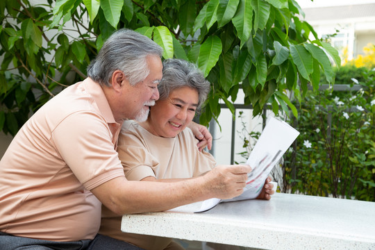 在front garden home的户外桌子上，一对亚洲老年夫妇一边看报纸一边大笑