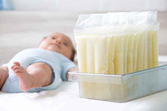 储存袋中冷冻的母乳和躺在背景上的婴儿