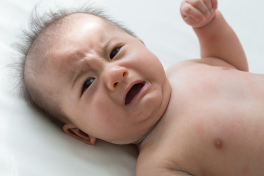 婴儿哭闹有绞痛症状，新生儿悲伤，婴儿尖叫，饥饿的母乳喂养在白色的床上