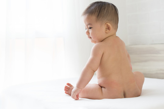 裸体的亚洲男婴坐在家里的白色床上