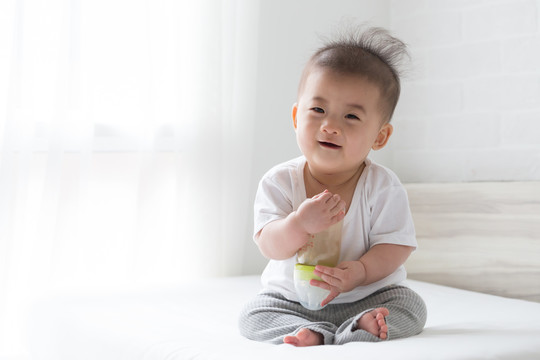 亚洲男婴拿着奶瓶坐在白色的床上