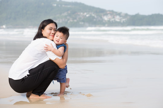 亚洲妈妈抱着男婴坐在沙滩上