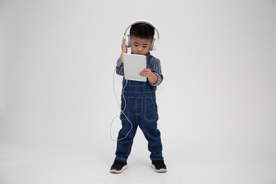 一个心满意足的可爱小孩的肖像，手持平板电脑，在应用程序上听音乐，背景为白色