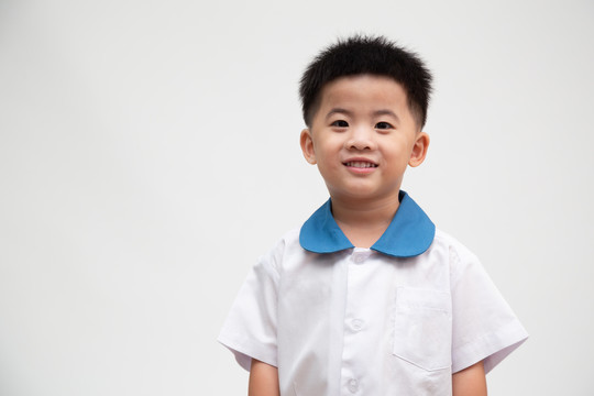 开朗微笑的亚洲小男孩，穿着白色背景的学生制服，上幼儿园第一天回到学校，泰国男孩模型