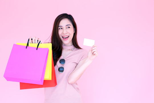 美丽的亚洲女性在情人节购物，快乐美丽的女孩喜欢用信用卡，拿着购物袋在粉色背景下的打折促销节上购物