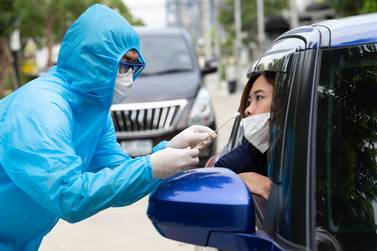 穿着PPE防护服的护士或穿着全套防护装备的医务人员从车内女司机处采集样本。冠状病毒2019冠状病毒疾