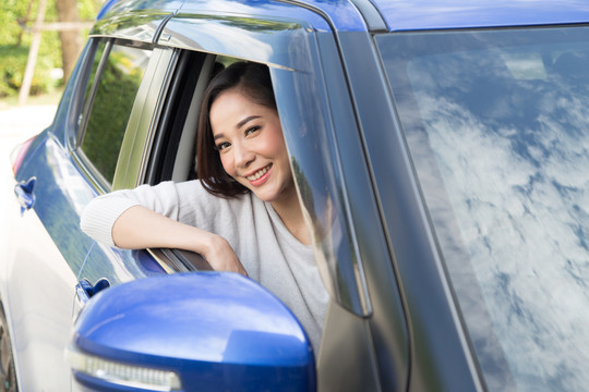 年轻的亚洲女性开车，开心地笑着，脸上带着快乐的积极表情。在开车去旅行的过程中，人们享受着欢笑的交通和