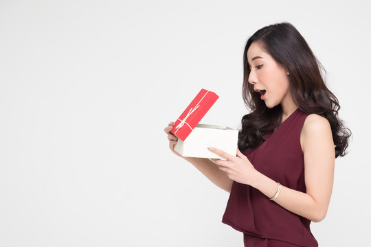 亚洲女性手持并展示红色礼盒，打开礼盒，在白色背景上表现出惊喜的表情