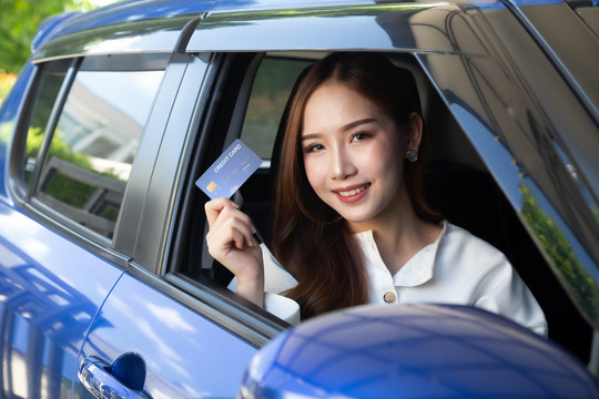 一名年轻的亚洲女子驾驶着一辆汽车并持有信用卡