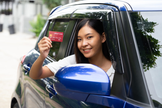年轻的亚洲女人拿着信用卡坐在车里