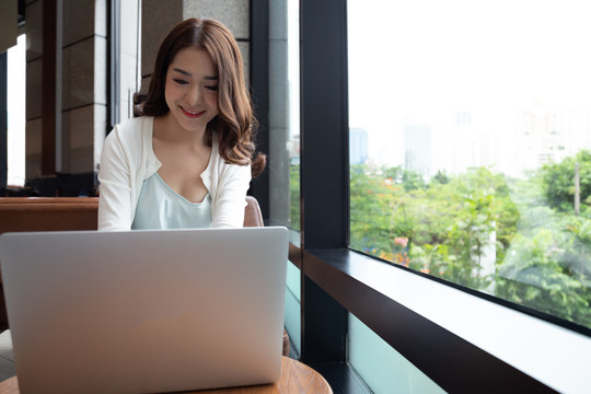 快乐的亚洲女性自由职业者在键盘笔记本电脑上与客户就在咖啡馆工作的项目打字