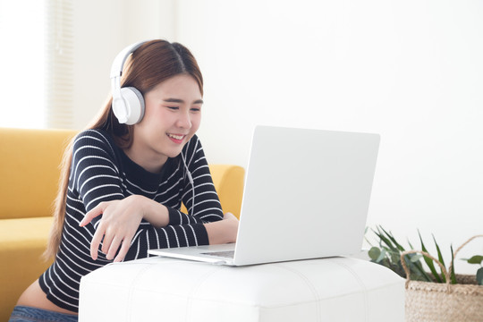 亚洲年轻女性对使用笔记本电脑学习在线课程的语言感到满意，微笑的女学生在笔记本电脑上听和看屏幕电子学习