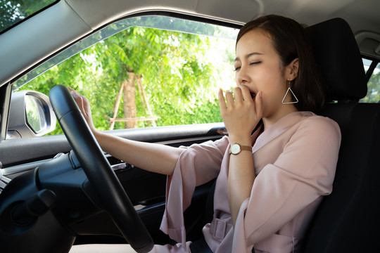 一位亚洲职业女性坐在车里，一边开车一边打哈欠