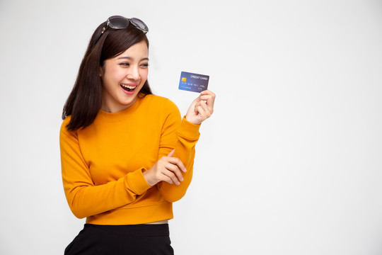 穿着黄色衬衫的快乐亚洲女性，持有信用卡或现金预付款，支付而不是金钱，并为女士卡提供特别策划的福利