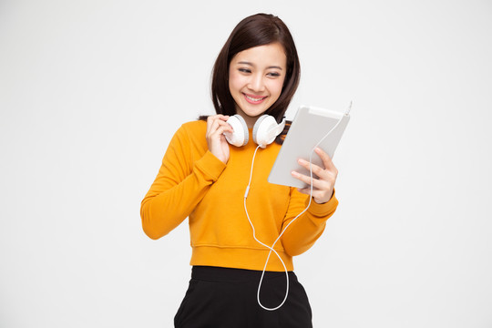 美丽的年轻亚洲女性，戴着耳机，穿着鲜艳的服装，在白色背景的平板电脑上欣赏歌曲旋律