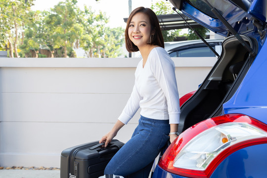 年轻的亚洲妇女正在把手提箱装进汽车的后备箱准备暑假旅行