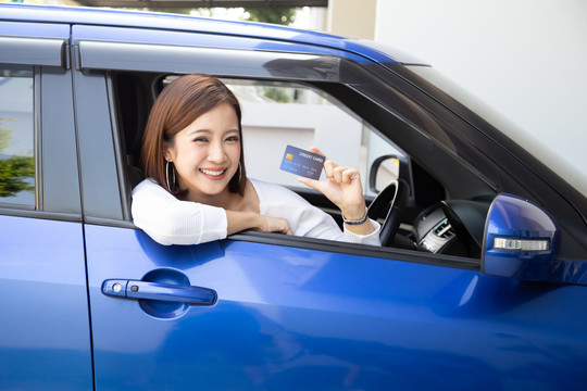快乐的年轻亚洲女性，持有支付卡或信用卡，曾在加油站支付汽油、柴油和其他燃料的费用，司机持车队卡为汽车