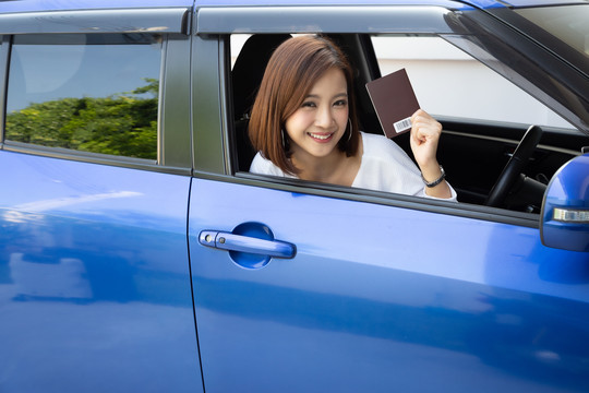 快乐的亚洲女人拿着护照本坐在车里，租车的外国游客概念