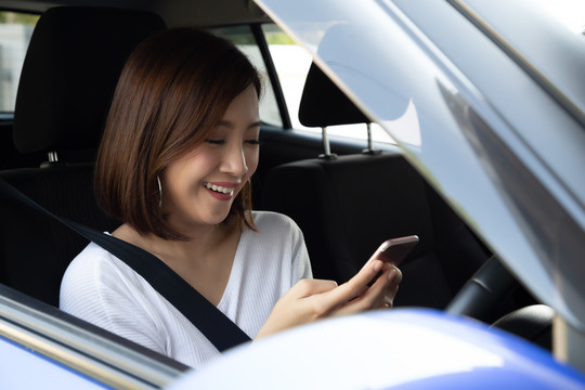 亚洲女性使用手机并在方向盘后发送信息，女性使用智能手机上的导航或应用程序驾驶汽车，智能技术概念