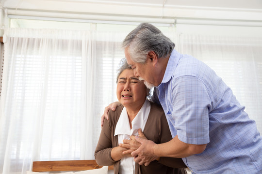 亚洲老年妇女，心脏疼痛，躺在客厅沙发上，由丈夫照顾，身体有问题，感觉不舒服