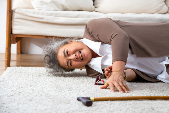 亚洲老年妇女跌倒在地毯上，躺在家里客厅的地板上，老年人摔倒