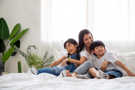 亚洲家庭的幸福与母亲、儿子和女儿在卧室的白色床上拥抱母亲，感受幸福与家庭关系理念