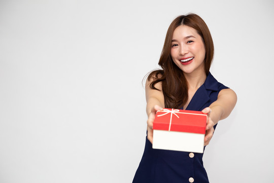 快乐美丽的亚洲女人微笑着，白色背景上隔着一个红色的礼盒。少女坠入爱河，接受情人的礼物。新年、圣诞节和