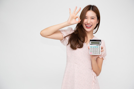 年轻的亚洲女性手持计算器，背景为白色，有商业账户和金融概念