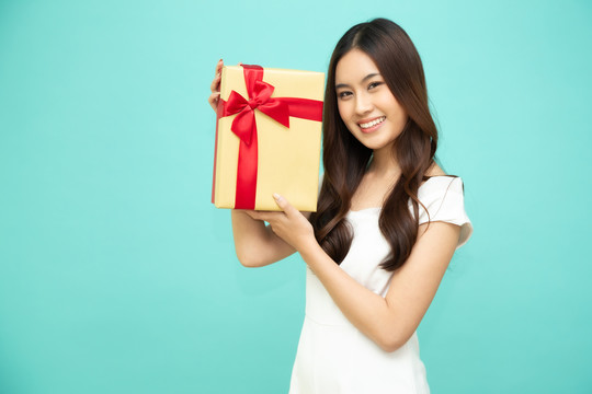 快乐美丽的亚洲女人微笑着，金色礼盒孤立在浅绿色背景上。少女坠入爱河，接受情人的礼物。新年、圣诞节和情