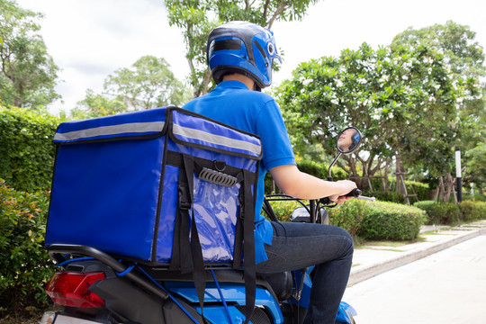 身穿蓝色制服的送货员骑着摩托车和送货箱。摩托车送食品快递服务理念