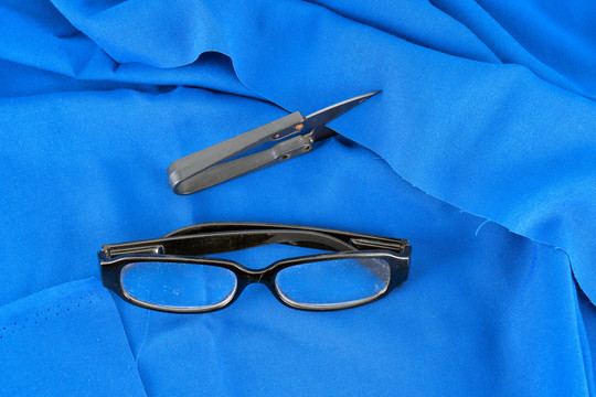 蓝色布料背景上的剪刀和眼镜