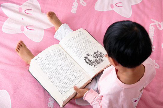 坐在床上认真看书的小女孩