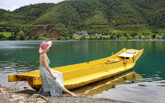 一位女人坐在泸沽湖岸边的木船上