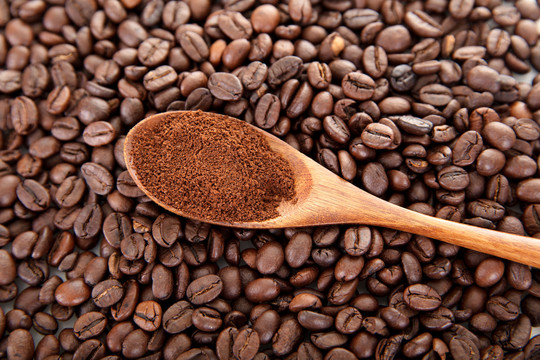 咖啡豆背景上的一勺咖啡粉