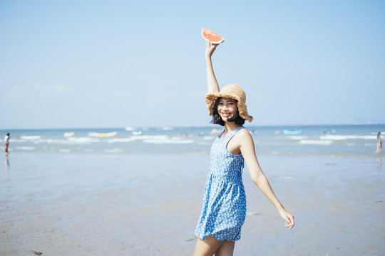 可爱的黑发女孩拿着一片西瓜在海边的海滩上嬉戏。