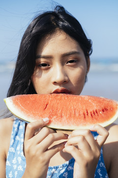 Cloae up在海滩上吃红色西瓜的可爱黑发女孩的肖像照。