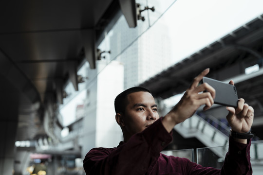 身着红衫的光头男子举起智能手机，与天空火车站上的人们合影留念。