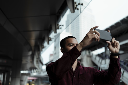 身着红衫的光头男子举起智能手机在城市里拍照。