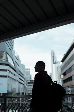 清晨，身穿红衫的光头男子走在天桥上，走进他的办公室，剪影拍摄。