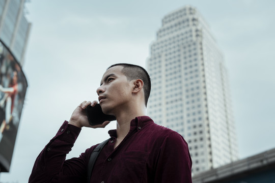 在高楼林立的城市里，穿着红衬衫的光头帅哥用智能手机进行低角度拍摄。